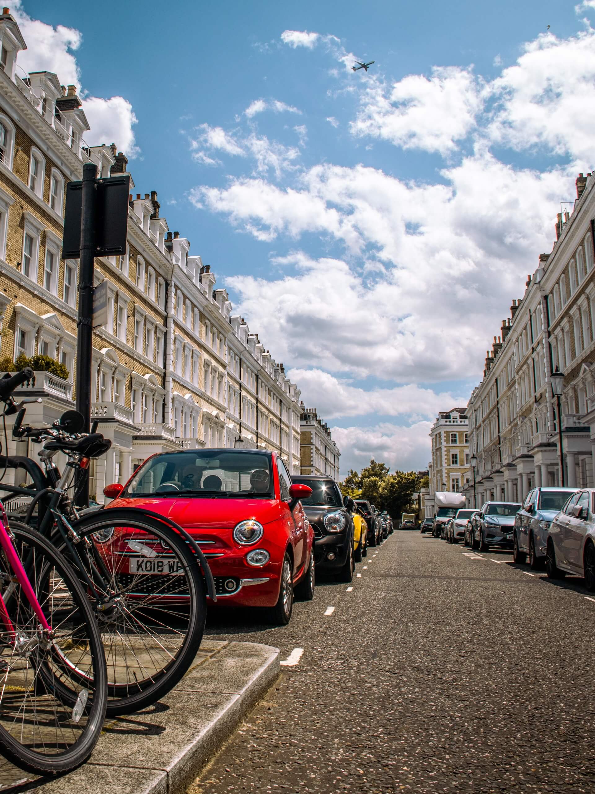 Image of London street with red car in foreground and plane in the sky